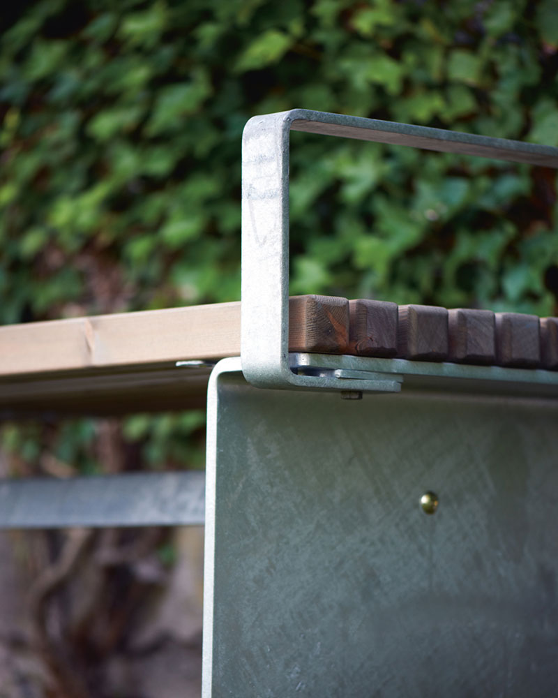 A close up image of a park bench detailing the wood, the steel and the armrest that makes up the bench.